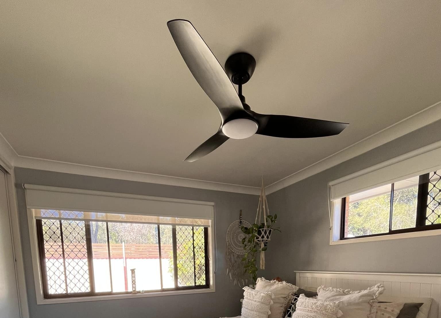Black ceiling fan installed in modern bedroom with large windows.