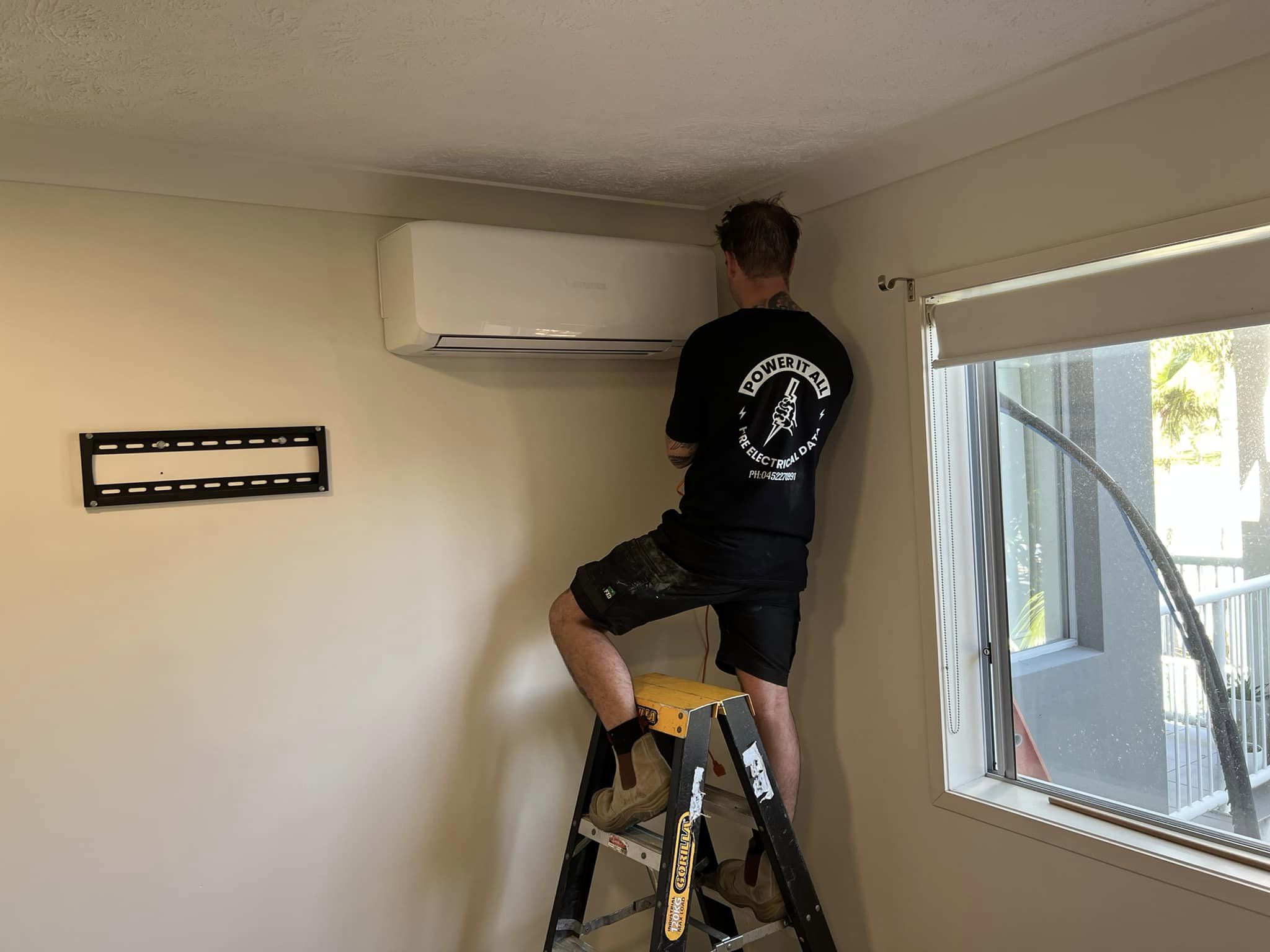 Electrician installing split system air conditioner on interior wall.